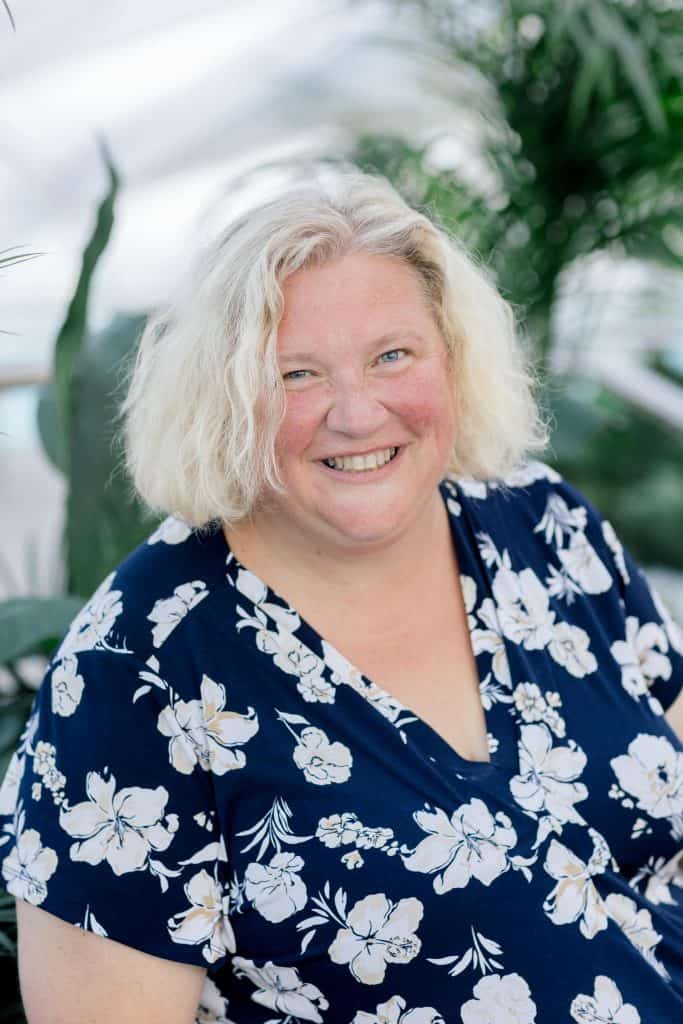 Smiling woman with curly blonde hair in floral shirt outdoors.