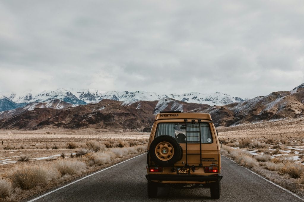 Vintage van on open road with mountain landscape in background.